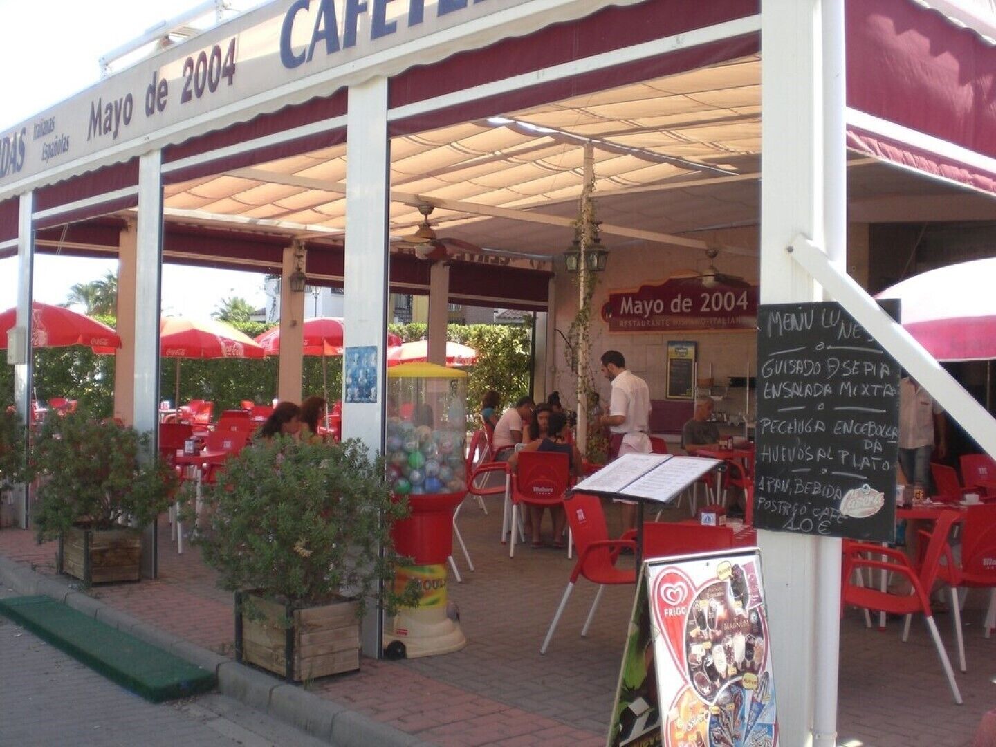 Ein Café im Freien mit roten und weißen Sonnenschirmen, Tischen und Stühlen.