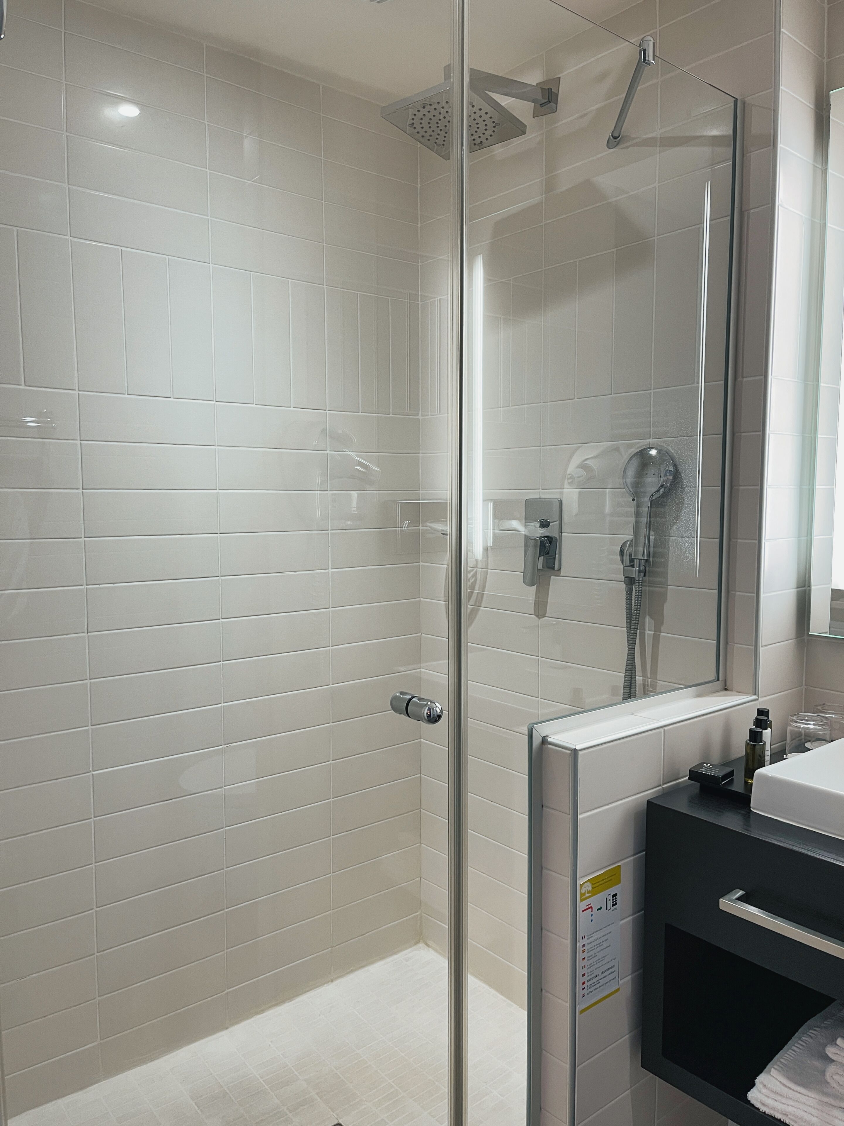 A modern bathroom with white tiles, a glass shower enclosure, and a black vanity with a mirror.