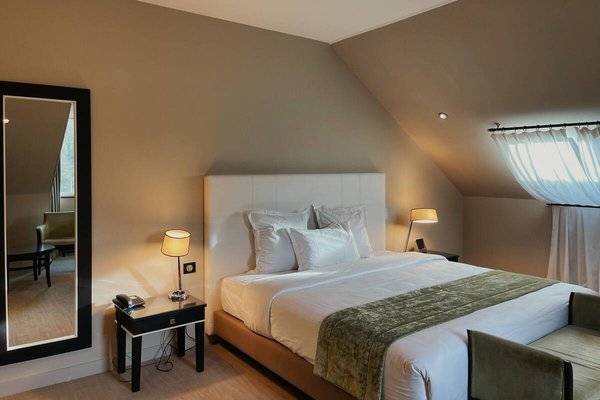 A modern hotel room with a large bed, a desk with a telephone, a mirror, and a chair.