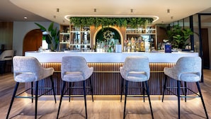 A bar area with four bar stools, a wooden floor, and a green plant arch above the bar. - Amicitia (L'Isle-Adam)