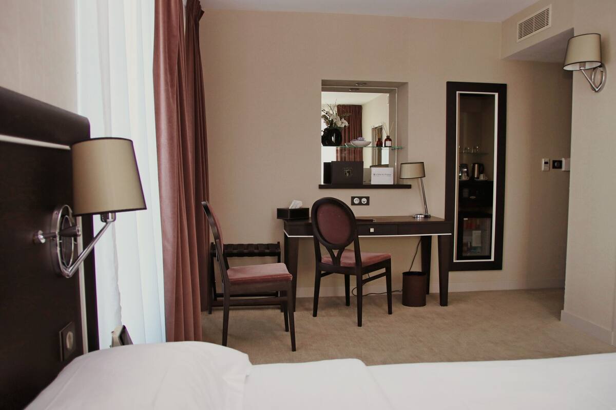 A hotel room with a bed, a desk, a chair, a mirror, and a lamp.