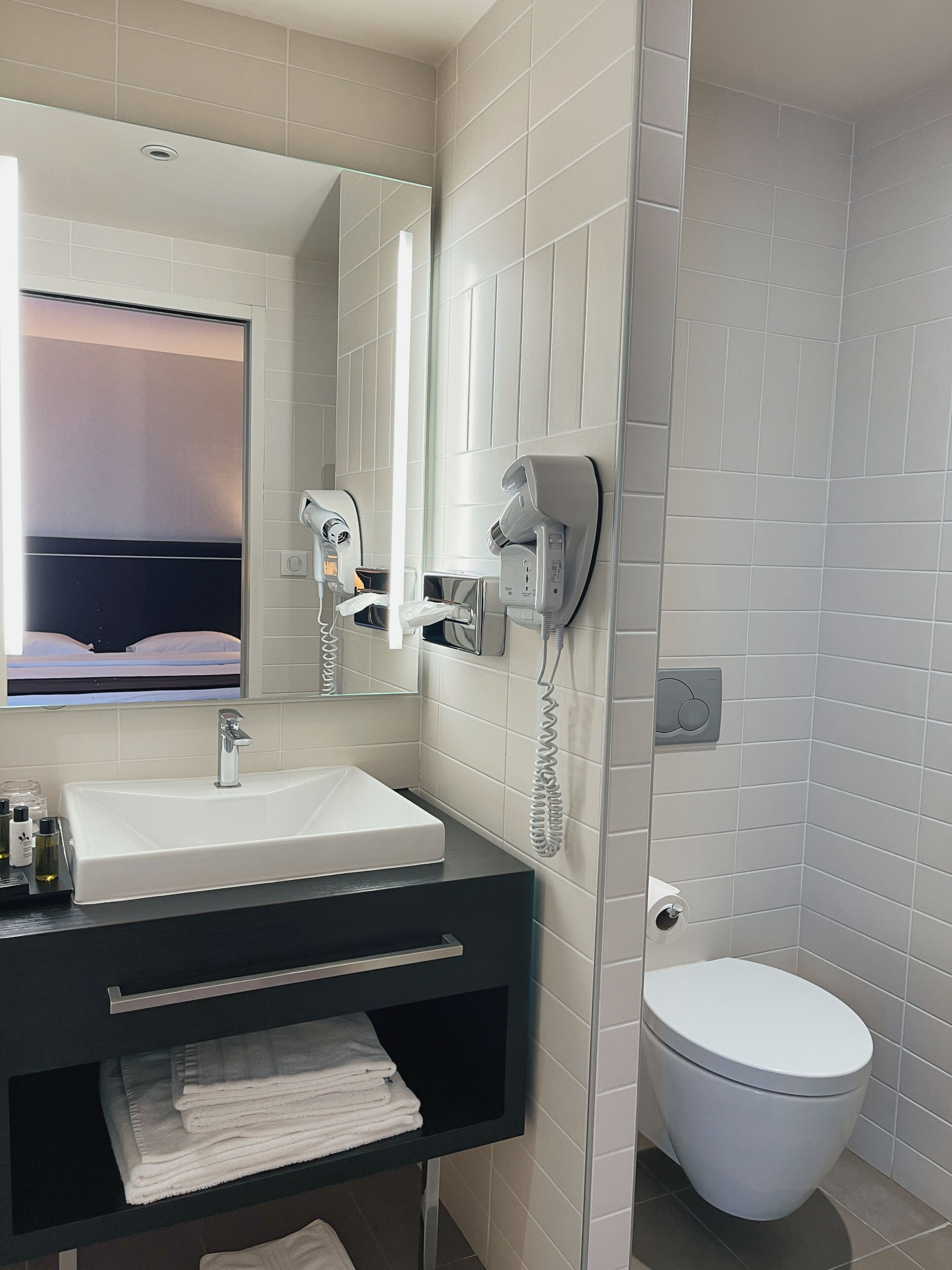 A modern bathroom with a white sink, a mirror, a hairdryer, and a toilet.