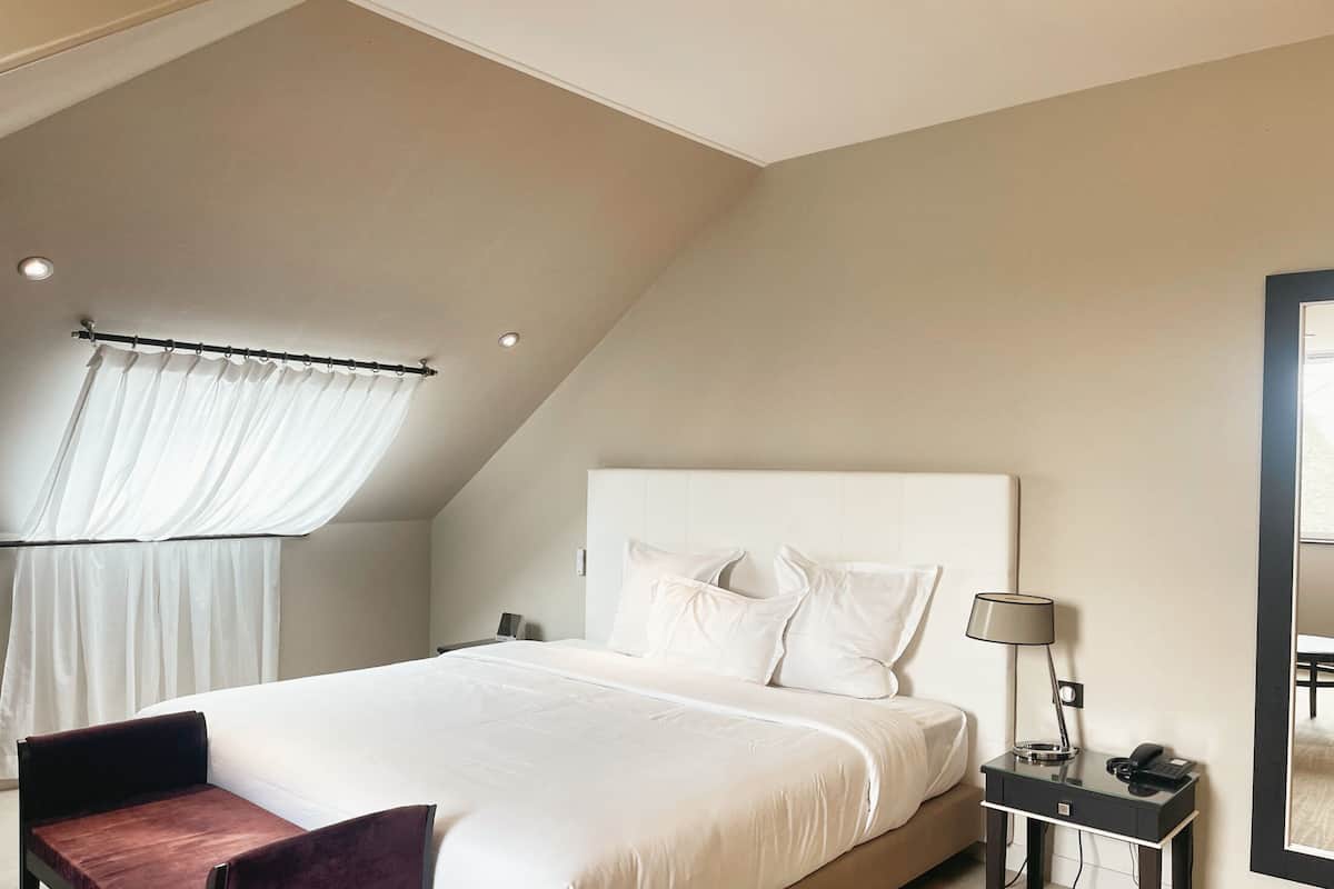 A modern bedroom with a large bed, a desk with a lamp, and a window with curtains.
