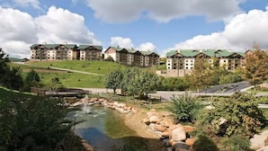 A hotel complex with multiple buildings, a small pond with a bridge, and a hilly landscape. - Smoky Mountains 1 Bedroom Deluxe (Sevierville)