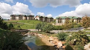 A hotel complex with multiple buildings, a small pond with a bridge, and a hilly landscape.