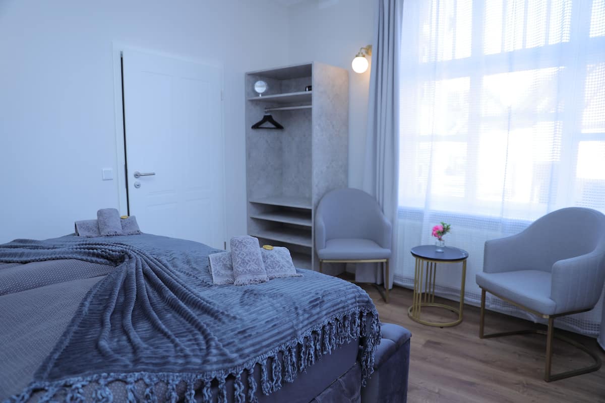 Ein modernes Schlafzimmer mit einem großen Bett, einem Kleiderschrank, zwei Sessel und einem kleinen Tisch.