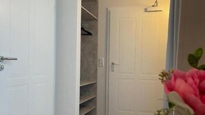 Um corredor com uma porta branca, um armário com prateleiras e um vaso com flores.