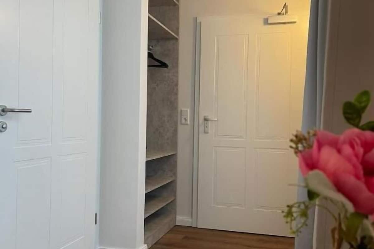 Ein Flur mit einer weißen Tür, einem Schrank mit Regalen und einer Vase mit Blumen.