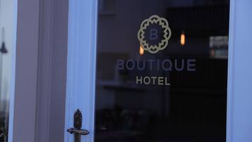 Ein Hotel Eingang mit einer Tür und einem Logo mit dem Buchstaben 'B' und dem Schriftzug 'BOUTIQUE HOTEL'.