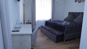 Um quarto moderno com um sofá-cama cinzento, uma pequena mesa de cabeceira e uma escrivaninha com uma cadeira.