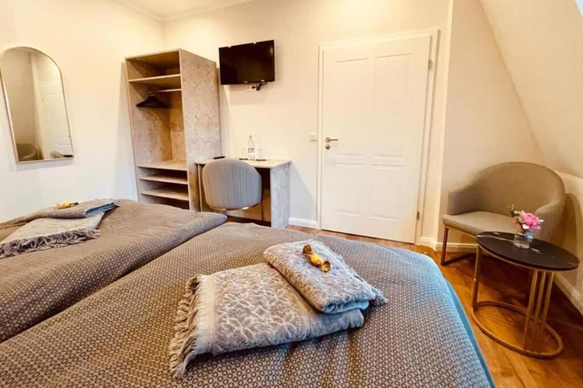 Ein Schlafzimmer mit zwei Betten, einem Fernseher, einem Schreibtisch und einem Sessel.