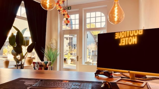 Quarto de hotel com escrivaninha, computador e iluminação decorativa.