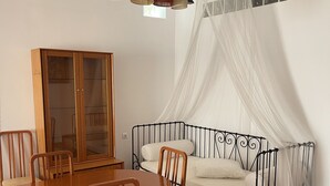 Un comedor con mesa y sillas de madera, un aparador con puertas de vidrio, una cama con dosel y una escalera.