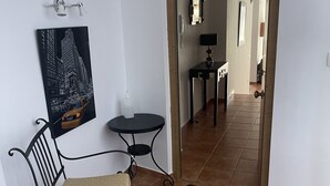 Un pasillo con una silla, una mesita, un espejo y una puerta que da a otra habitación.