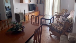 Una sala de estar con una mesa de comedor de madera, sillas, un sofá, un televisor y un armario.