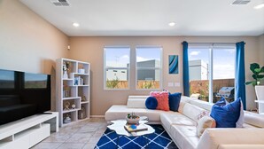 A modern living room with a flat-screen TV, white sofas, a coffee table, and a bookshelf.