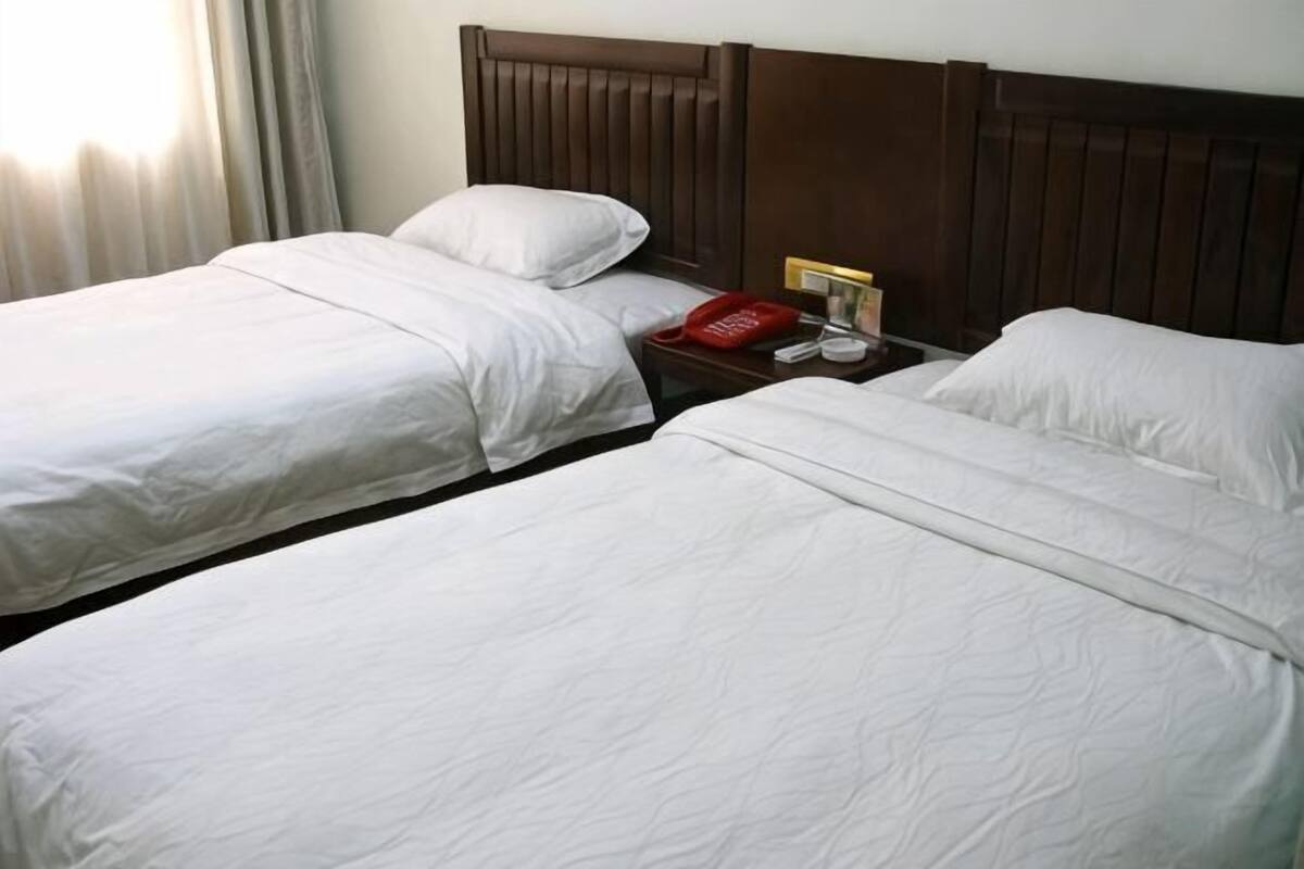 A hotel room with two beds, a wooden headboard, a nightstand with a telephone, and a window with curtains.