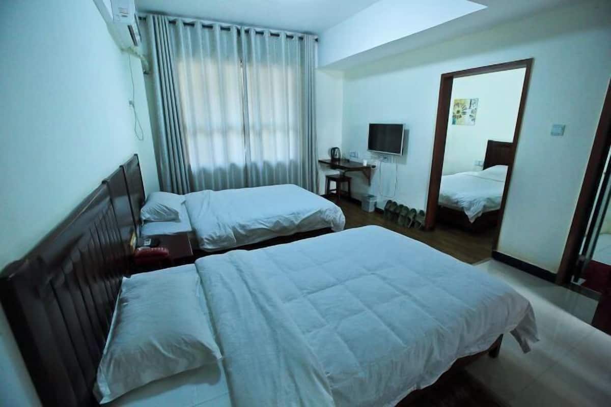 A hotel room with two beds, a desk with a chair, a television, and a mirror.
