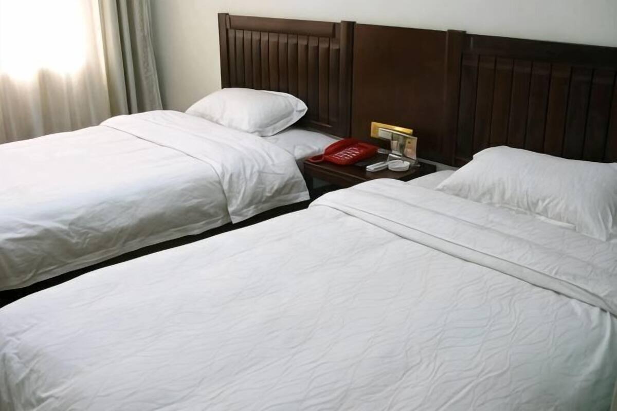 A hotel room with two beds, a wooden headboard, a nightstand with a telephone, and a red basket.