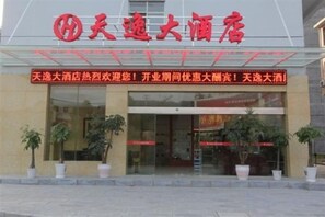 A hotel entrance with a prominent red sign, potted plants, and a glass door. - Tianyi Hotel Zhangjiajie (Zhangjiajie)