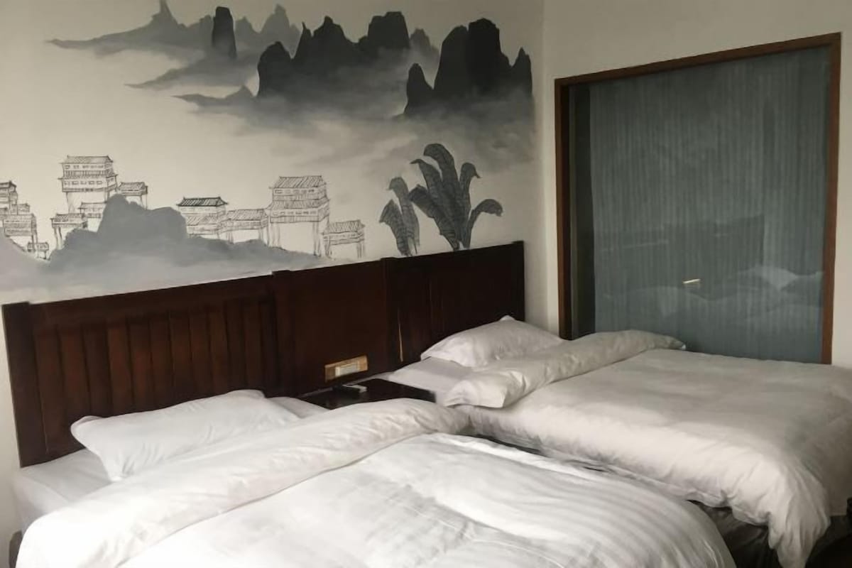 A hotel room with two beds, a wooden headboard, and a wall mural depicting traditional architecture and nature.