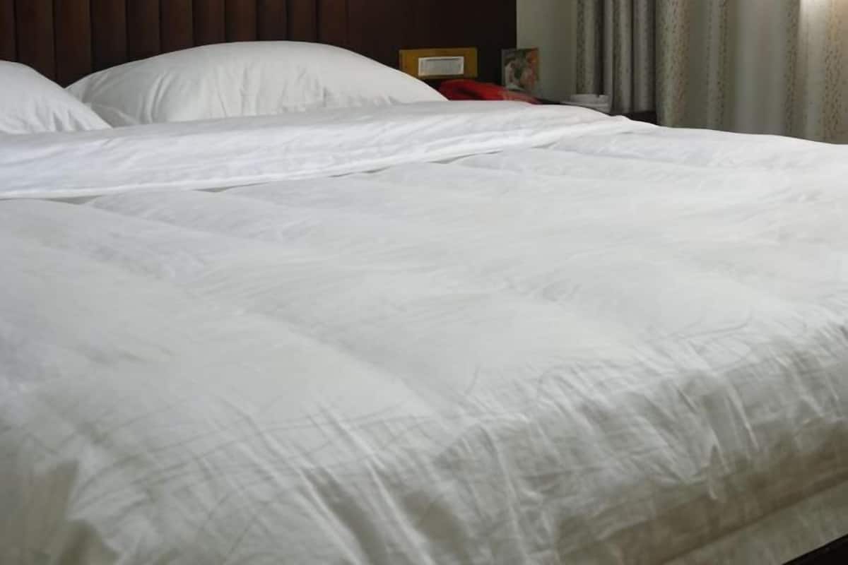 A neatly made bed with white bedding, a wooden headboard, and a bedside table with a lamp.