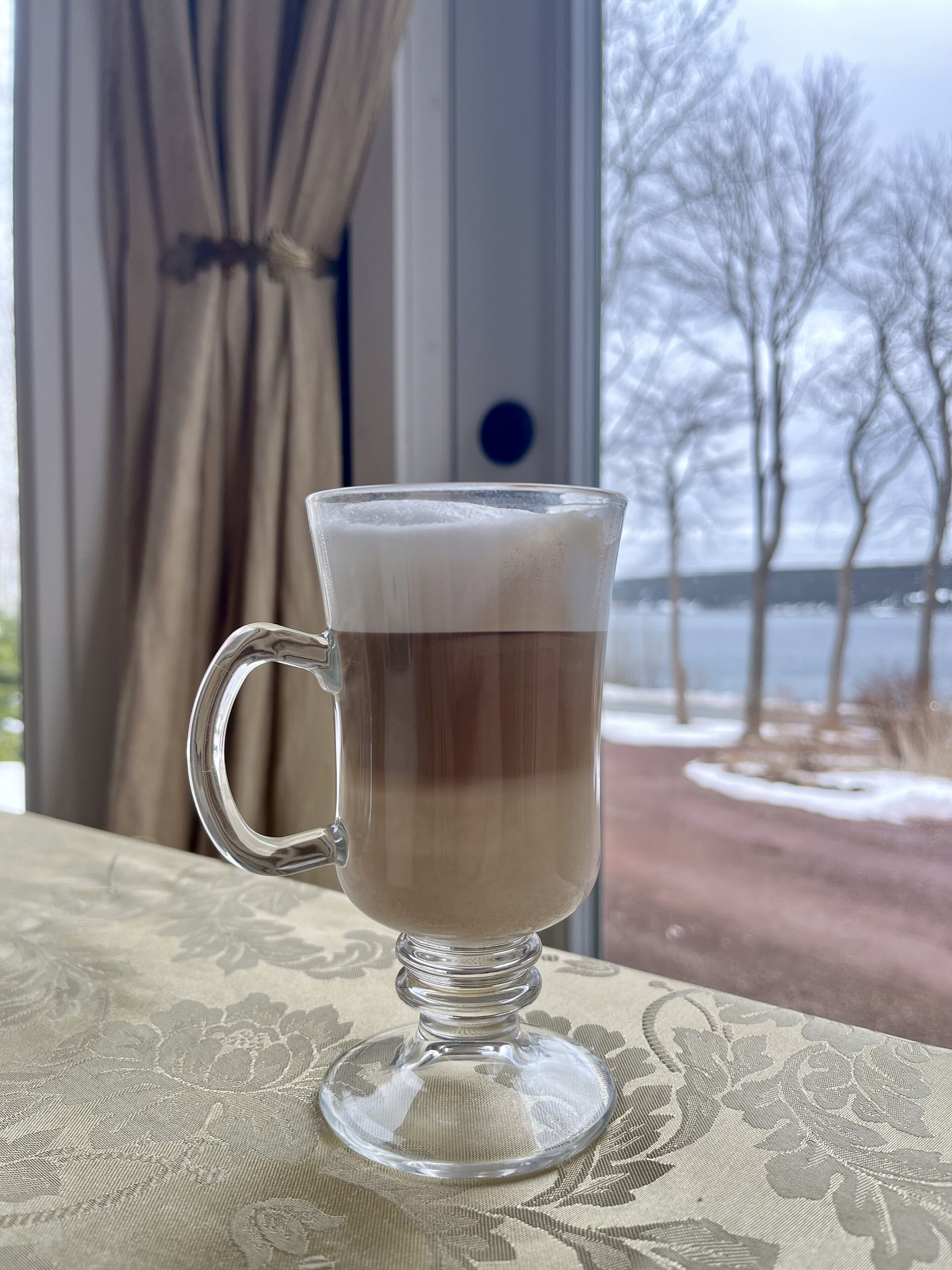 A clear glass mug with a layered beverage on a table with a floral pattern.