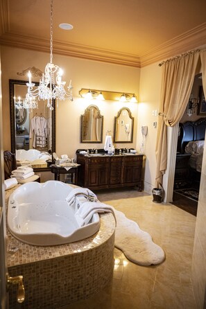 A luxurious bathroom with a large bathtub, a chandelier, a vanity with a mirror, and a robe rack.