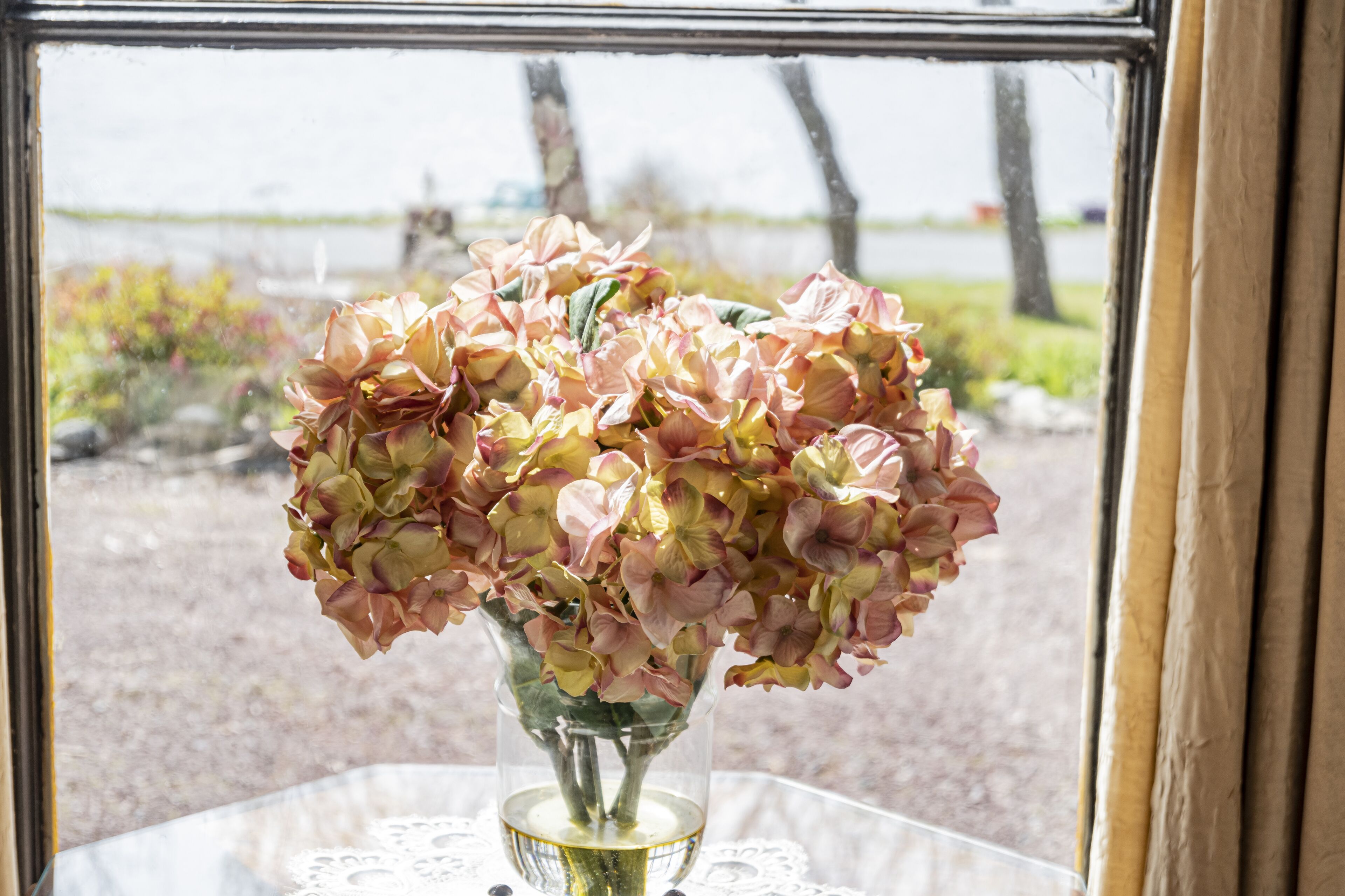 A vase with flowers on a table by a window.