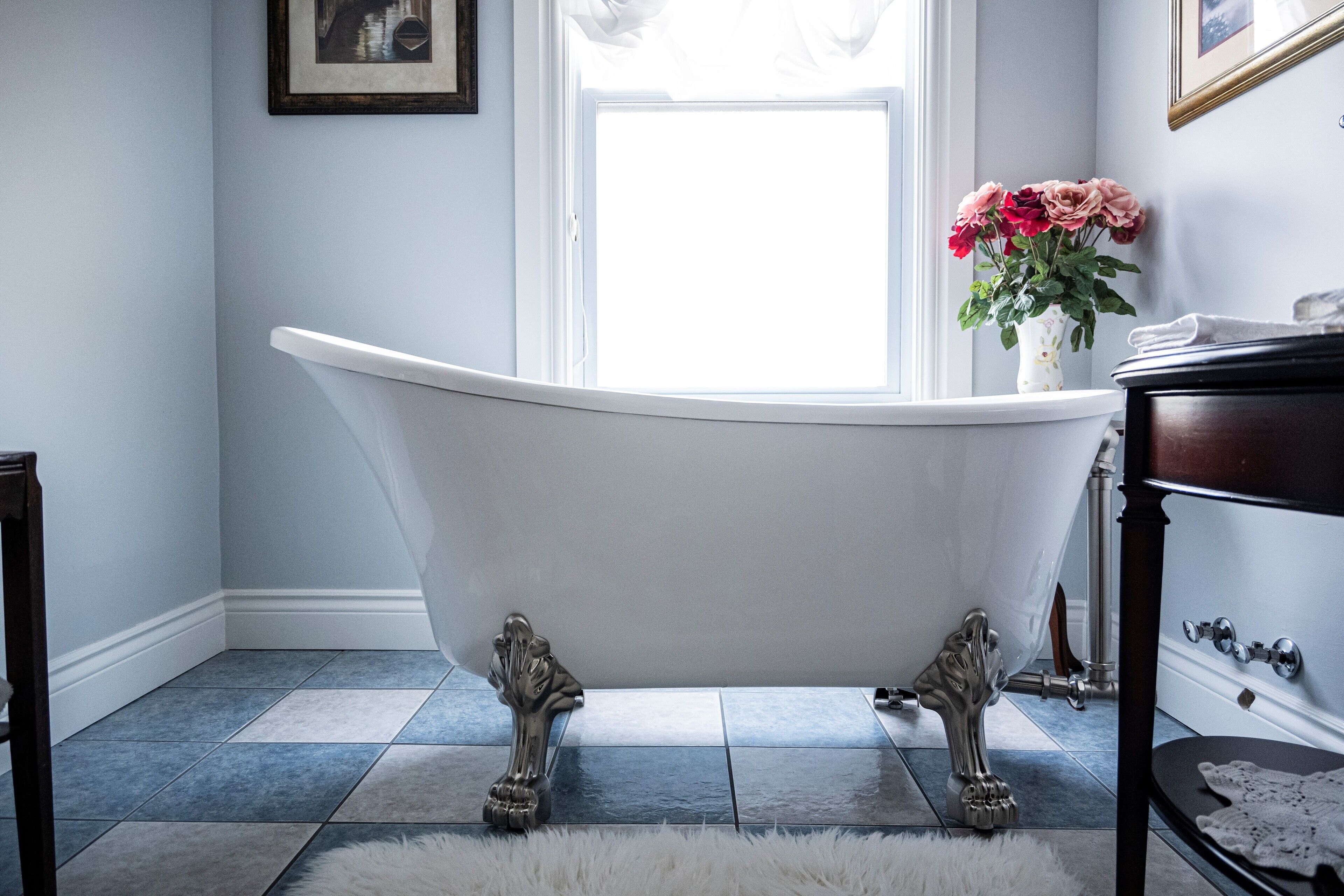 A bathroom with a freestanding bathtub, a white fluffy rug, and a vase with flowers on the windowsill.