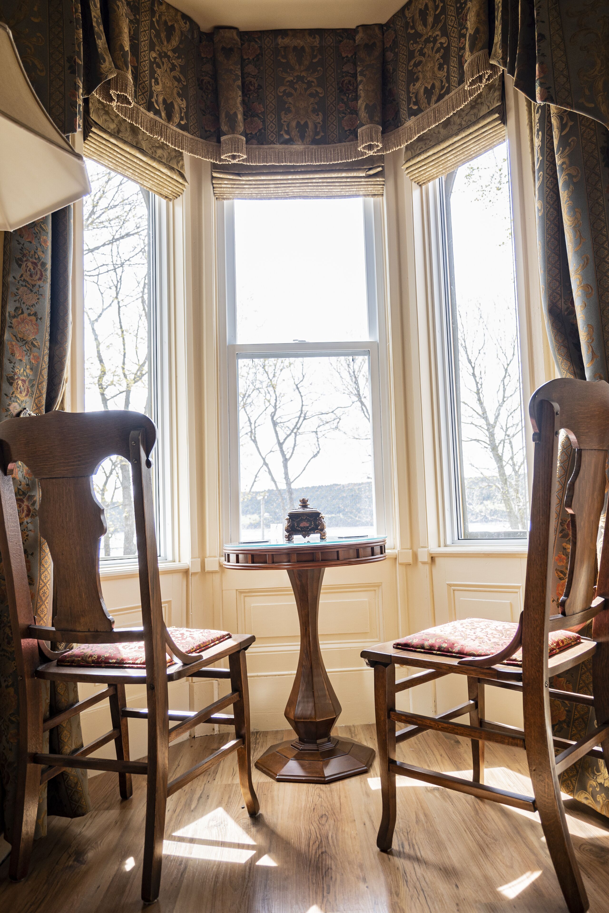 A corner room with two wooden chairs, a small table, and a view through a large window.