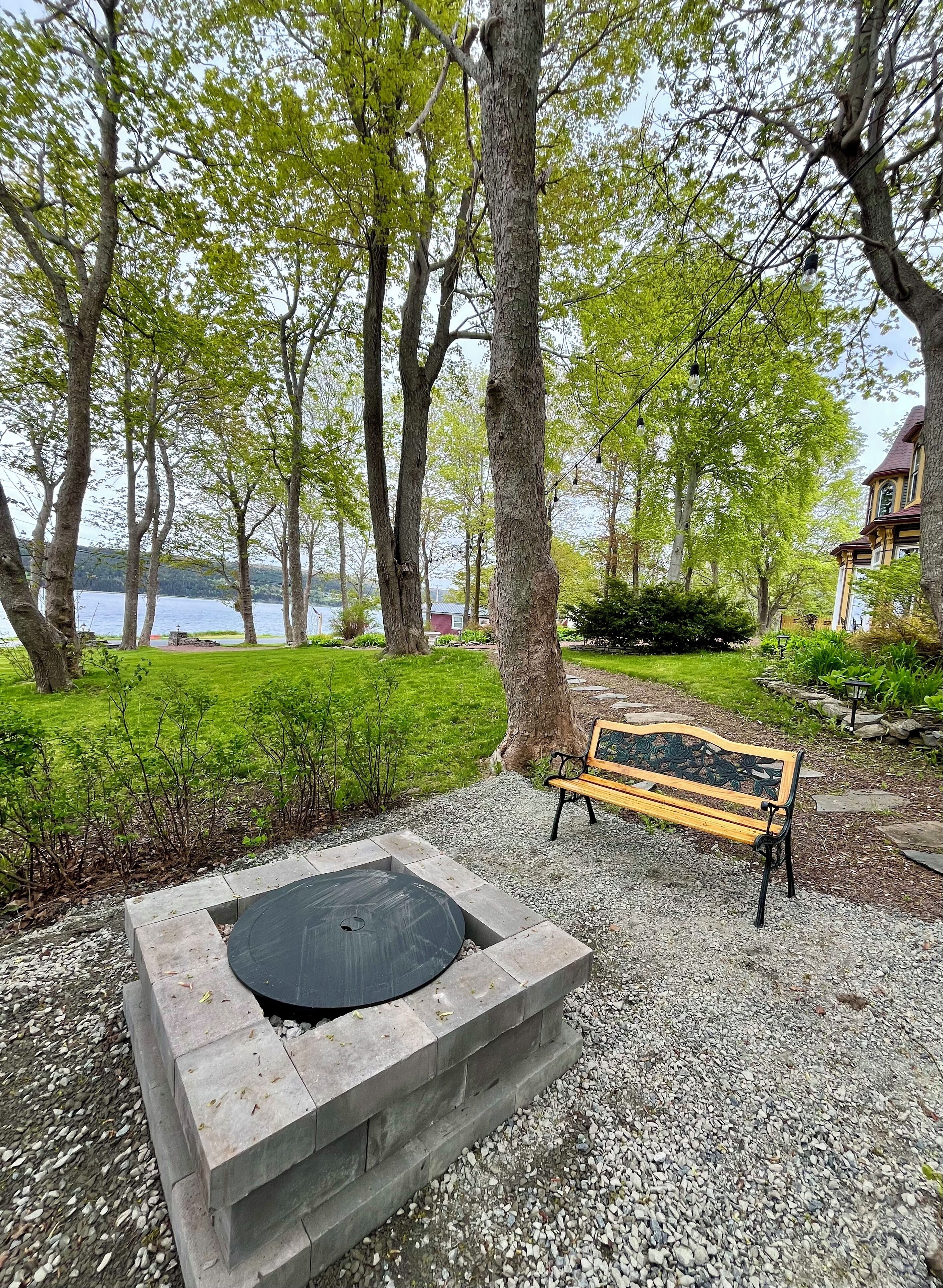 A park with a stone fire pit, a wooden bench, and a lake view.