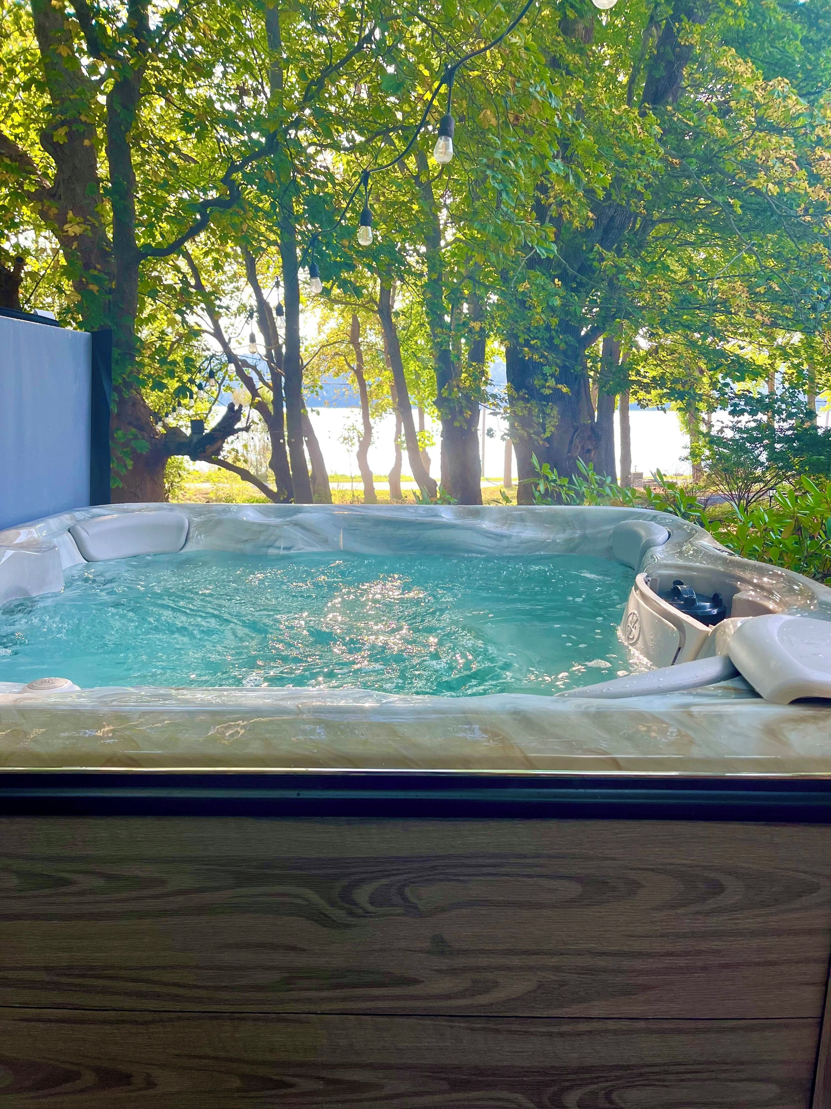 Een hottub omringd door bomen met uitzicht op een waterpartij op de achtergrond.