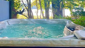 Een hottub omringd door bomen met uitzicht op een waterpartij op de achtergrond.