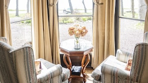 Ein Zimmer mit zwei Polstersesseln, einem kleinen runden Tisch und Blick auf einen See durch große Fenster mit Vorhängen.