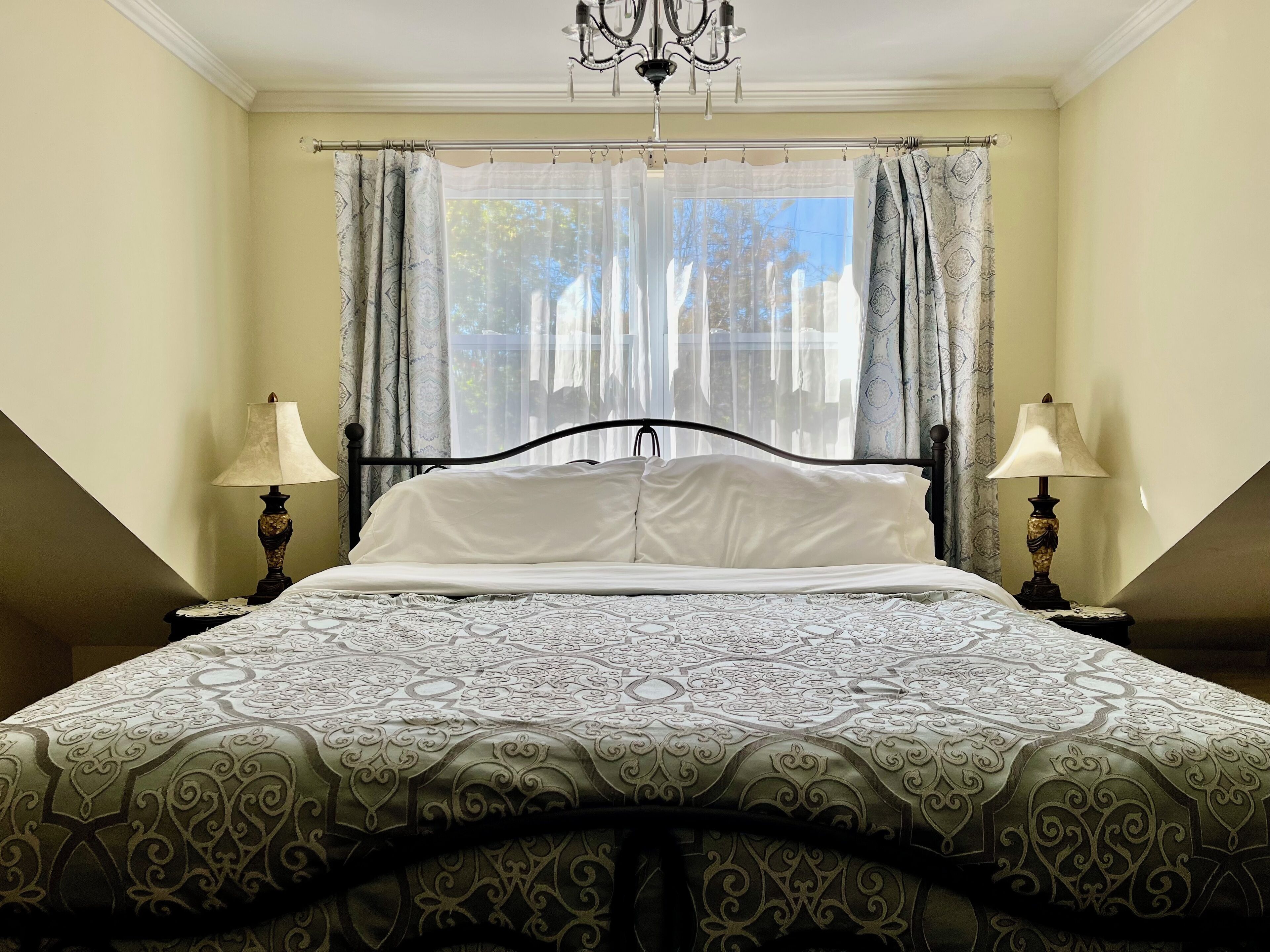 Un dormitorio con una cama, dos lámparas de noche, un candelabro y una ventana con cortinas.