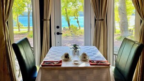 Ein Essbereich mit Tisch für zwei Personen, Blick auf einen See und Vorhängen an den Fenstern.