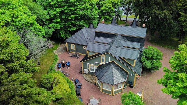 Ein zweistöckiges Haus mit Terrasse, umgeben von dichten Bäumen und Blick auf einen See.