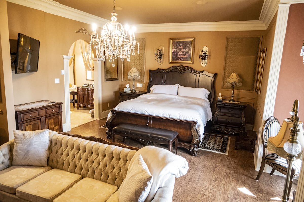 A spacious bedroom with a large bed, a chandelier, and a classic design.