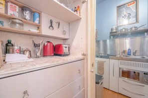 A kitchen with a white countertop, a red kettle, and a microwave.