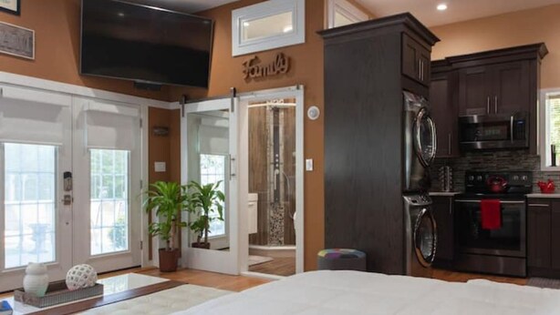 A modern kitchen with dark cabinetry, a microwave, and a stove. There is a large flat-screen TV mounted on the wall.