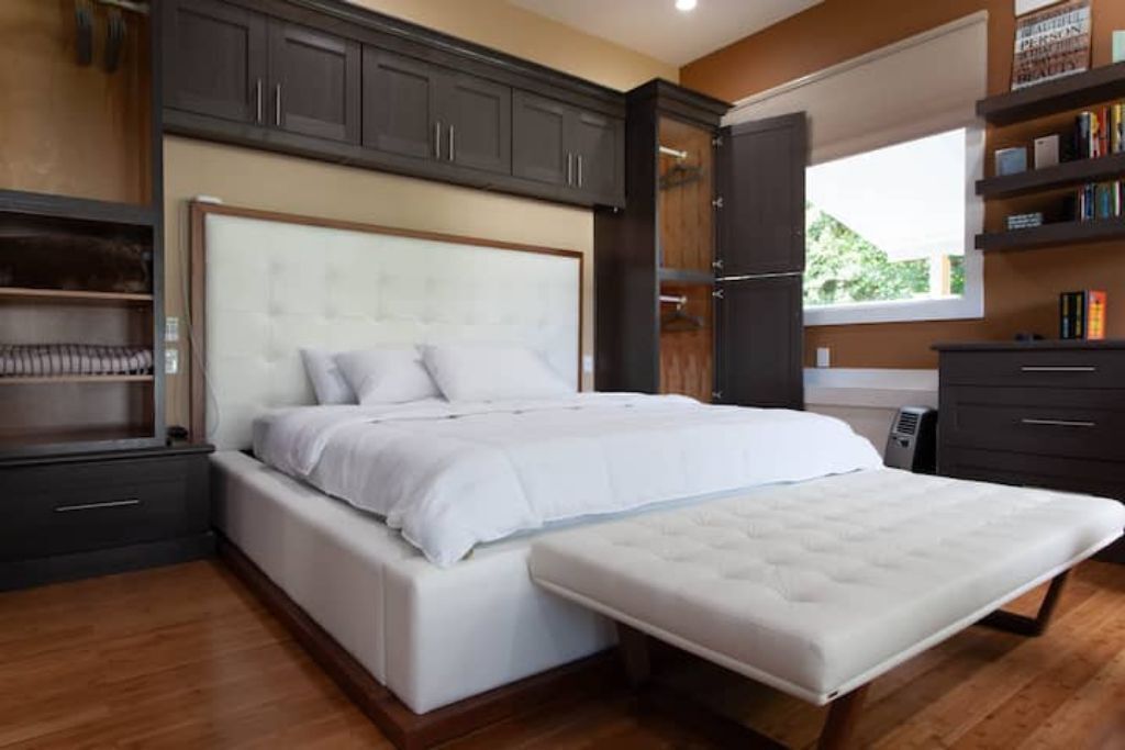 A modern bedroom with a large bed, built-in shelving, and a window with a view.