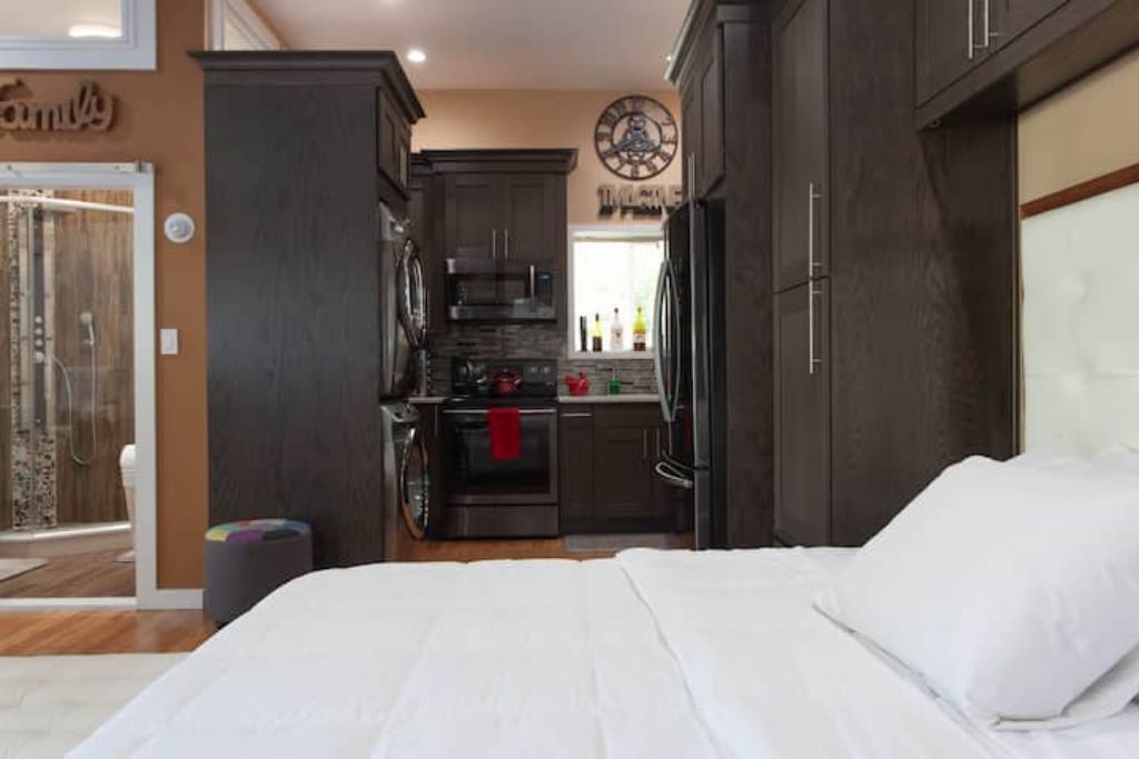 A compact bedroom with a large bed, a small kitchenette, and a bathroom with a shower.