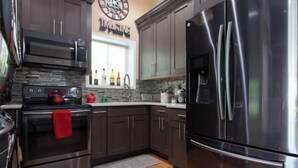 A modern kitchen with dark cabinets, stainless steel appliances, a red kettle, and a backsplash with bottles.