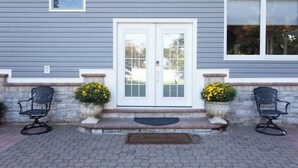 A house with a gray exterior, white double doors, and two potted plants with yellow flowers on either side of the entrance.