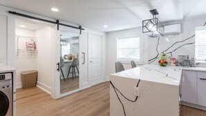 A modern kitchen with a marble countertop, a built-in oven, and a sliding door leading to a dining area. - Ultra-Modern Studio | Near Hospital & NYCIM | WiFi (Huntington)