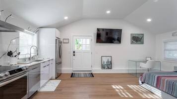 Una cocina moderna con electrodomésticos de acero inoxidable, un comedor con mesa de vidrio y un dormitorio con cama y ventana.