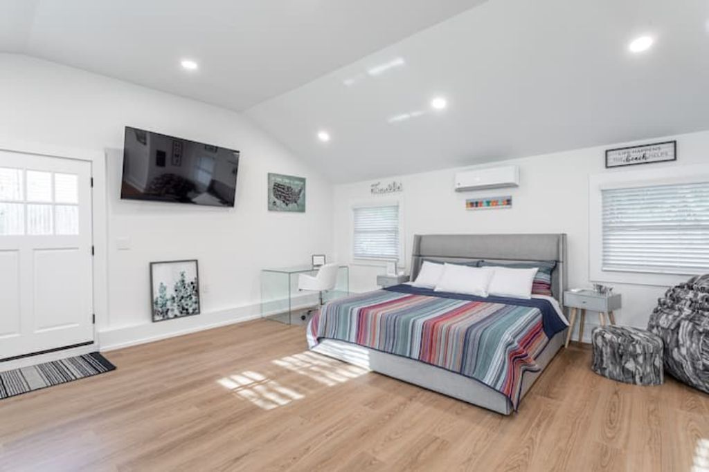 A modern bedroom with a large bed, a TV mounted on the wall, and a window with blinds.