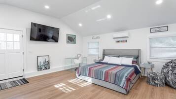 A modern bedroom with a large bed, a TV mounted on the wall, and a window with blinds.