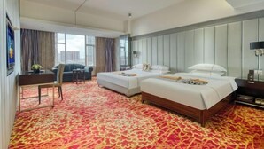 Hotellihuone, jossa on kaksi sänkyä, suuri ikkuna, punakuvioinen matto ja näkymä kaupunkiin.